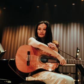 New Zealand singer Bic Runga holds a guitar under stage lights.