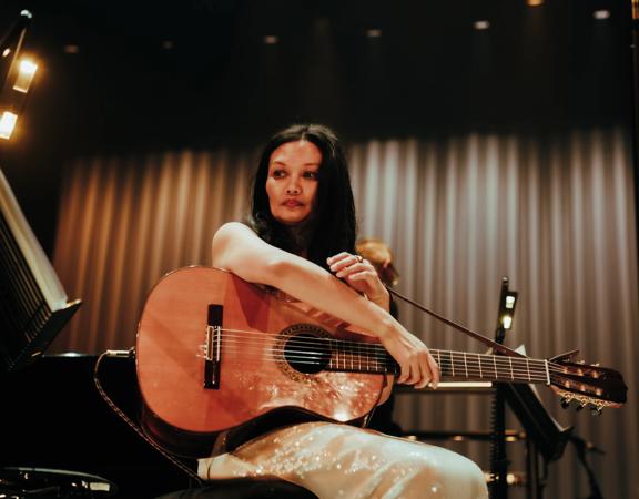 New Zealand singer Bic Runga holds a guitar under stage lights.