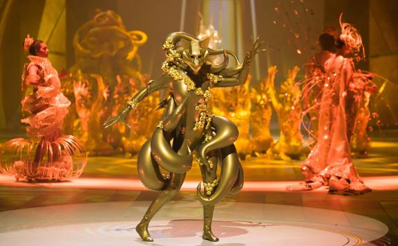 A winner from the World of WearableArt Festival 2023. The garment is made of a gold spandex material with tentacle elements wrapping around the model.