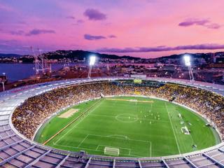 A birdseye view of Sky Stadium in Wellington, New Zealand during a soccer match under a pink sunset sky.